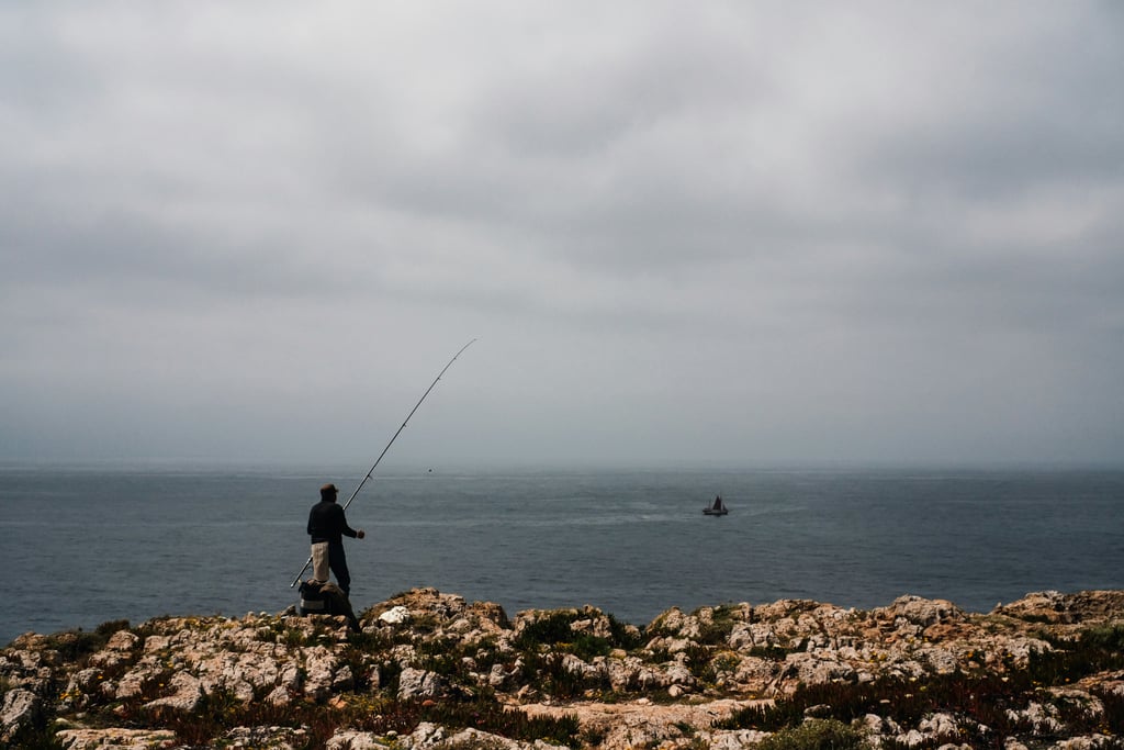 Traditional fisherman casting line from cliffs at Sagres on Rota Vicentina