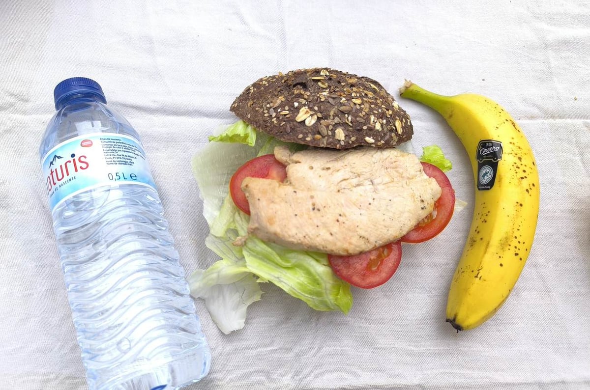 Traking Transfers Chicken Sandwich Pack on dark seeded bread with lettuce and tomato, banana and water bottle beside it