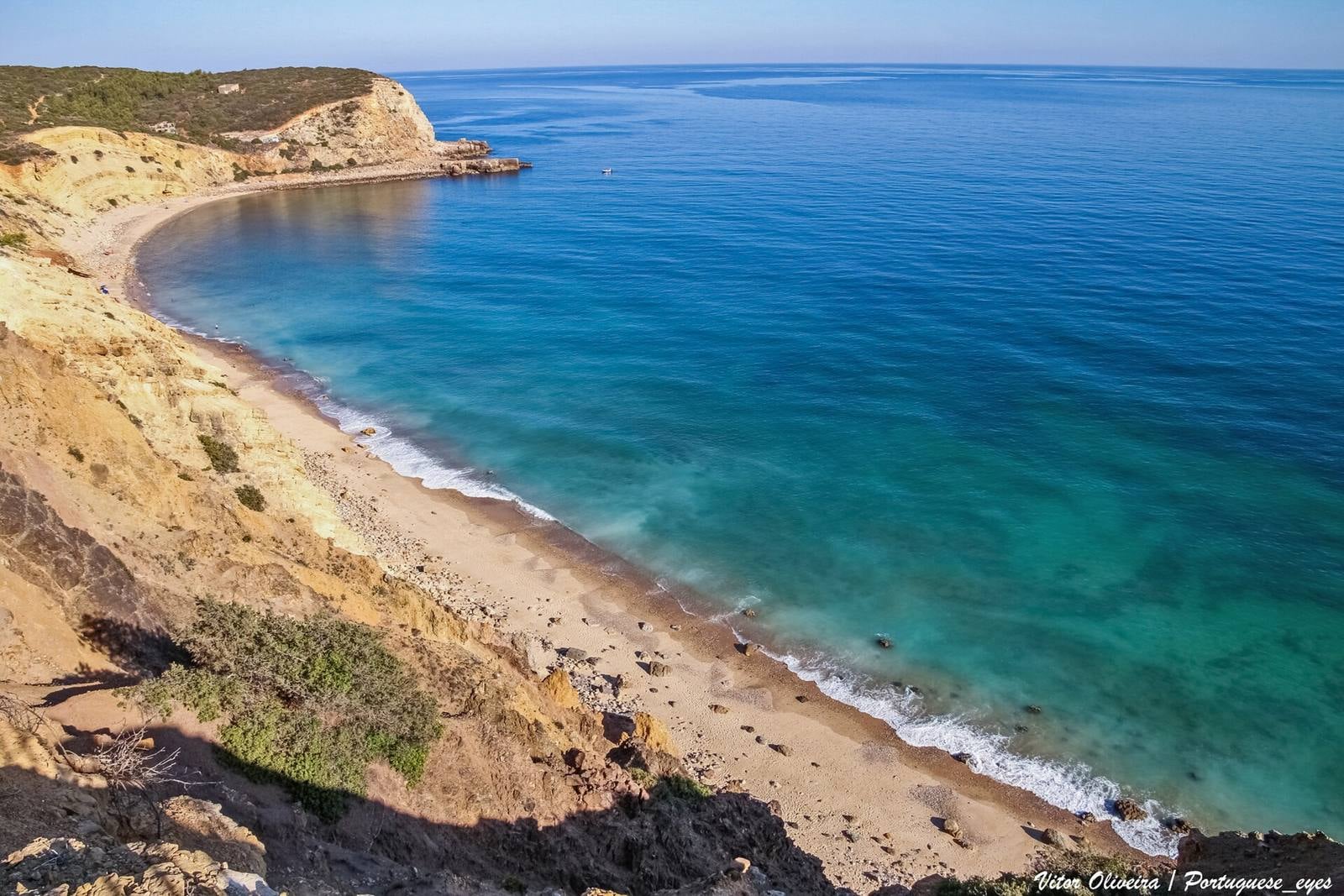 Praia das Cabanas Velhas seen from the cliffs: a curved bay of sand and pebbles with turquoise water