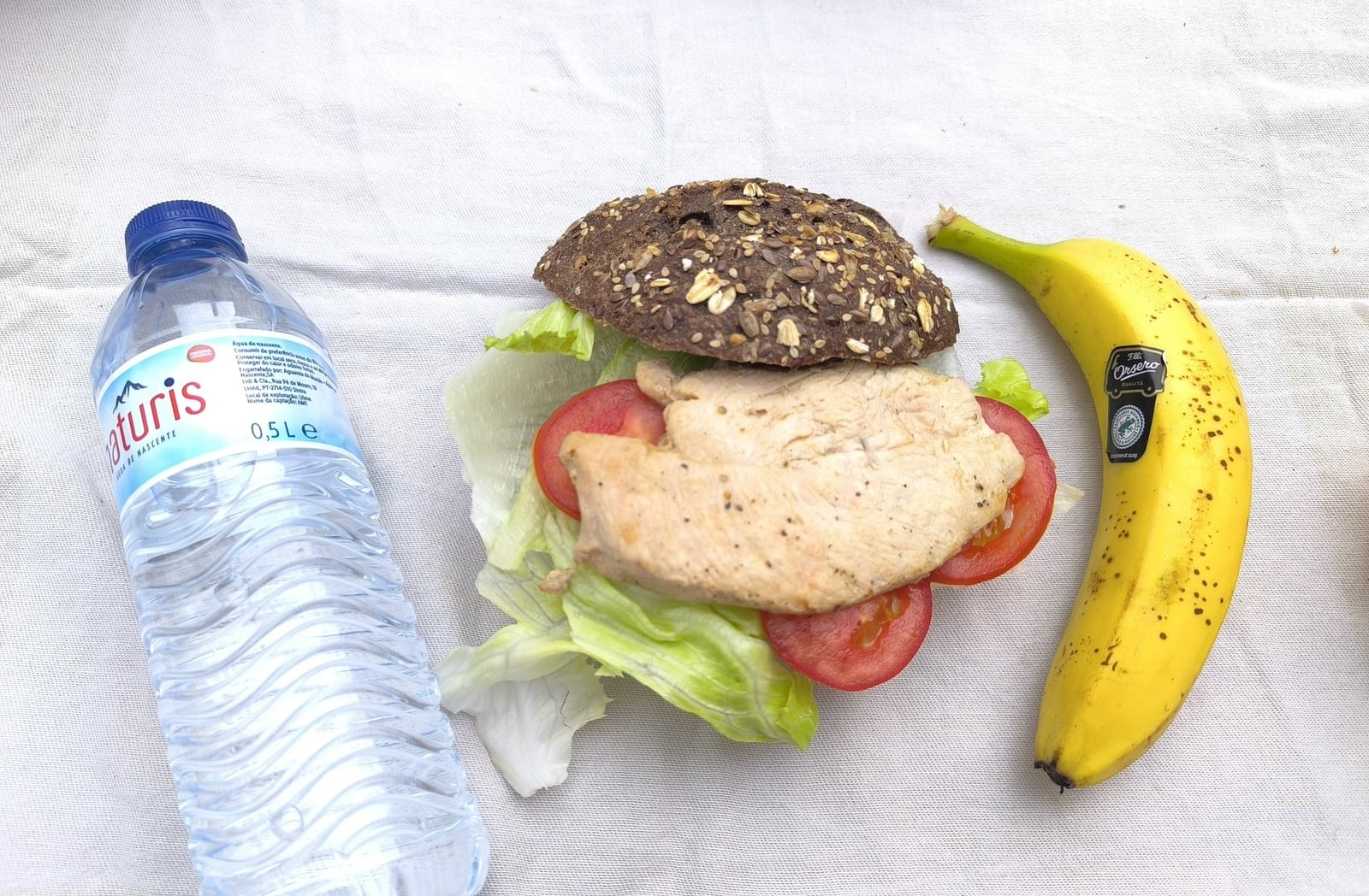 Traking Transfers Chicken Sandwich Pack on dark seeded bread with lettuce and tomato, banana and water bottle beside it